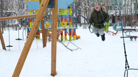 Dad rolls his son on a swing. A child rides on a swing in a winter park. Stock Footage 167679584