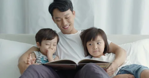 Dad is sitting in bed and playing with his little son and daughter Stock Footage 100936368