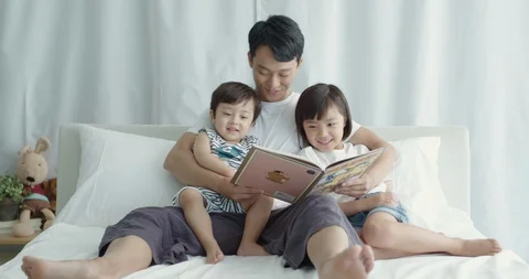 Dad sitting in bed and reading storybook to his son and daughter Stock Footage 100936274