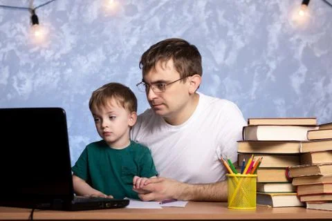 Dad with a small child sits at the table and looks at the laptop. Foto stock