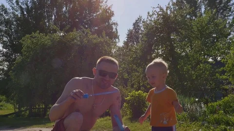 Dad in sunglasses blowing bubbles with son on nature slow motion Stock-Footage 80086447