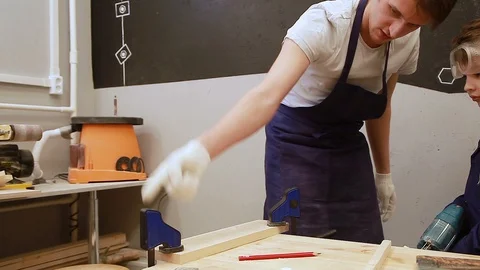 Dad teaches the boy in goggles to work as an electric jigsaw in the workshop Video stock 102240048