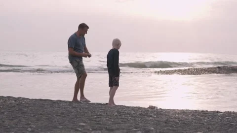 Dad teaches his son to throw stones in the sea on the beach at sunset in Sochi Stock Footage 142568425