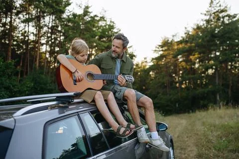 Dad teaching boy how to play guitar during summer camping adventure in nature. Stock Photos