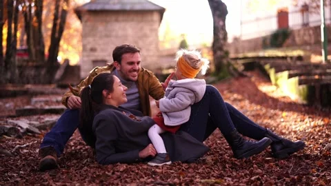 Dad throws fallen leaves over mom with a little girl sitting on her stomach Stock Footage 281453346