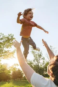Dad throws his laughing son high into the air in a green park 스톡 사진