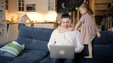 Dad is trying to work on laptop with two children cuddling him in living room. Stock Footage 146877154