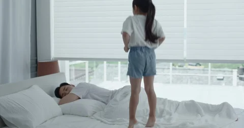 Dad waking up because of a daughter jumping on the bed Stock Footage 100938824