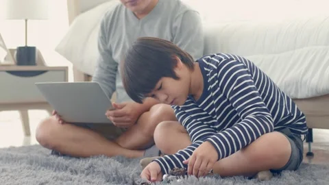 Dad working on laptop and talking his curious little son as playing with doll Stock Footage 142869894