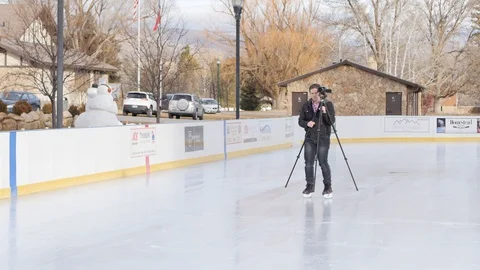 Daddy skates on ice with camera and tripod Stock Footage 85649887
