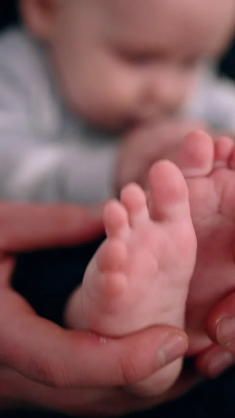 Dad's hands hold the tiny feet of his baby. Father tickles and claps son's feet. Stock Footage 318008358