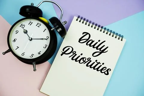 Daily Priorities text written on notepad with alarm clock flat lay on multi.. Stock Photos