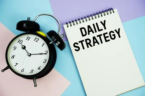 Daily Strategy text written on notepad with alarm clock flat lay on multico.. Stock Photos