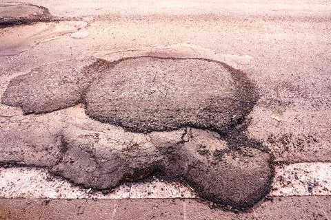 Damaged asphalt road showing multiple deep potholes Stock Photos