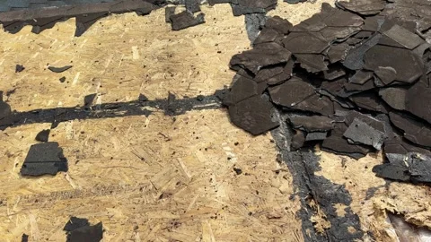 Damaged asphalt shingles scattered across exposed wooden roof decking during Stock Footage 346757361