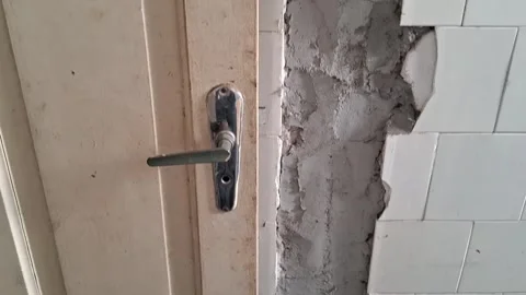 Damaged bathroom wall with broken white tiles and wooden door footage Stock Footage 339248173
