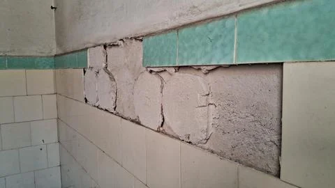 Damaged bathroom wall with missing ceramic tiles and exposed grey mortar Stock Photos