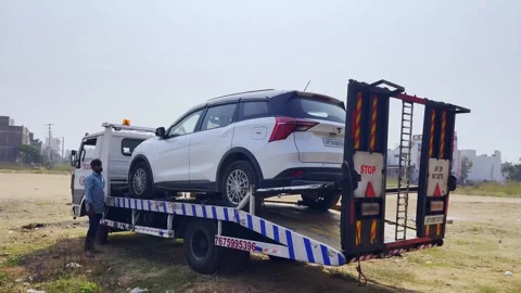 Damaged car being towed onto a flatbed tow truck with operator walking behind Stock Footage 332422573