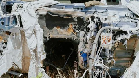 Damaged car chassis with exposed components in overgrown grass area Stock Photos