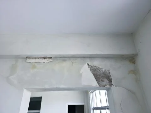 Damaged ceiling corner with collapsed plaster and peeling paint Foto stock