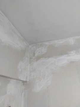 Damaged ceiling corner with plaster patches and damp stains Stock Photos