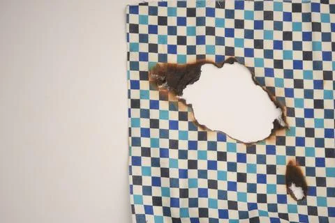 Damaged cloth with burn hole on patterned fabric surface Stock Photos