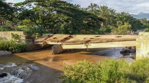 Damaged concrete bridge spanning brown river, reminder of the cr Stock Photos