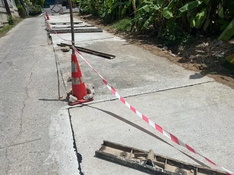 Damaged concrete road section marked with safety cone and red-white warning.. Stock Photos