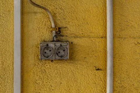 A damaged electrical socket on a dirty yellow wall, damaged electrical inst.. Stock Photos