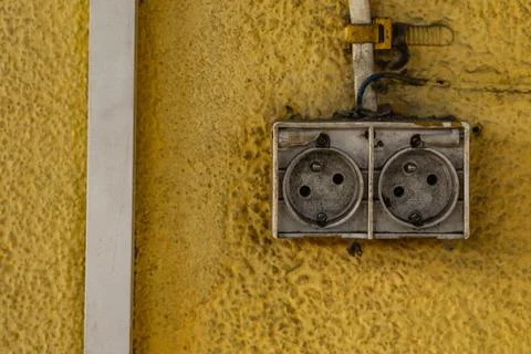 A damaged electrical socket on a dirty yellow wall, damaged electrical inst.. Stock Photos
