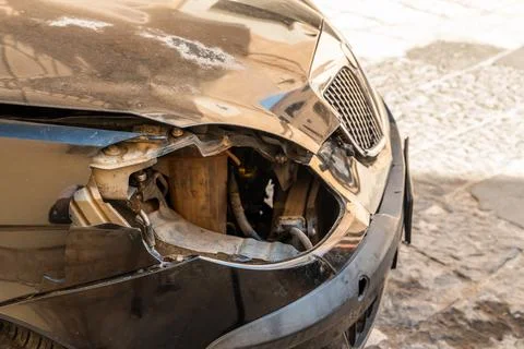 Damaged front bumper of a car with broken headlight and crumpled metal parked on Stock Photos