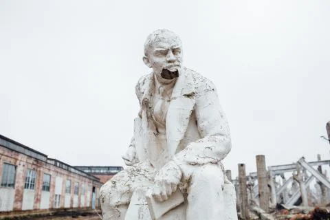 Damaged Lenin statue sitting on a chair with  book in his hand Stock Photos