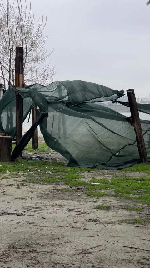 Damaged netting and posts along the riverside near a park on a cloudy day in Stock Footage 332132425