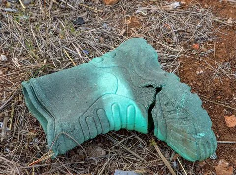 Damaged old green rubber boot lying abandoned on dry ground with cracked su.. Stock Photos