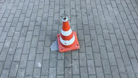 Damaged orange and white traffic cone on gray brick pavement Stock Footage 345327346