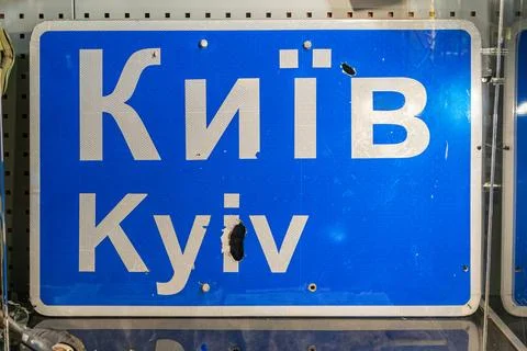 Damaged road sign in Cyrillic script, leaning against a metal grid structure, Foto stock