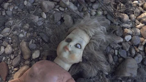 Damaged scary doll lying on river stone pebbles Vidéo 152647414