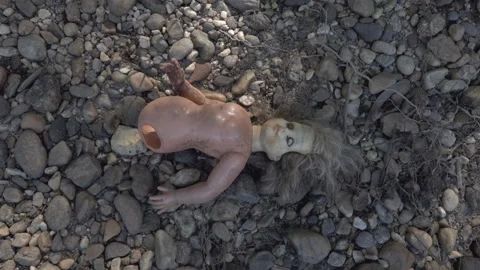 Damaged scary doll lying on river stone pebbles Vidéo 152647446