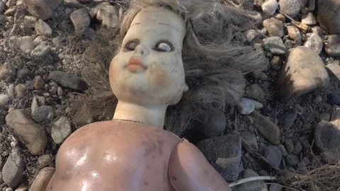Damaged scary doll lying on river stone pebbles Video stock 152647481