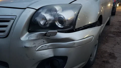 Damaged silver car with bumped bumper and headlight in parking lot post Vídeos de archivo 270054509