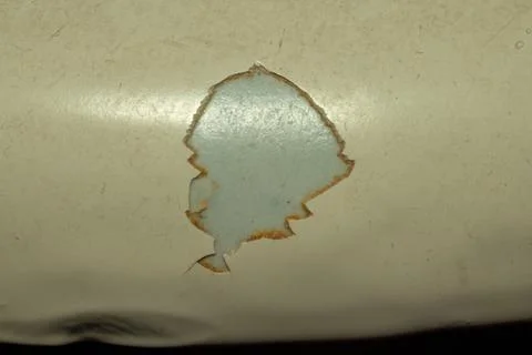 Damaged surface texture with a hole revealing underlying blue paint on metal Stockfoto's