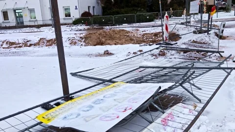Damaged temporary construction fence panels and warning sign lying on snowy Stock Footage 328089958