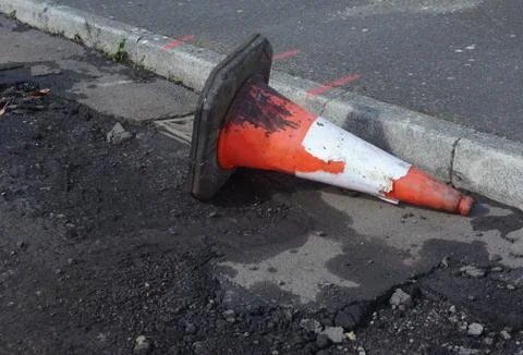Damaged traffic cone in gutter, road undergoing repairs Stock Photos