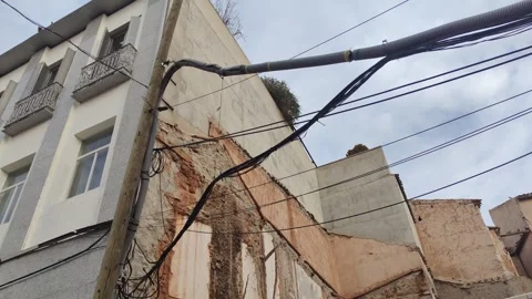 Damaged urban building facade and power lines against cloudy sky Vídeo Stock 340326659
