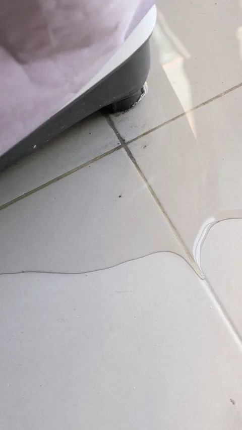 Damaged washing machine leaking clean water from its base and creating a large Stock Footage 333802359