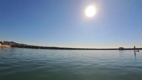 Dana Point Harbor breakwater and standup paddleboarder on calm water under sun Stock Footage 331549257