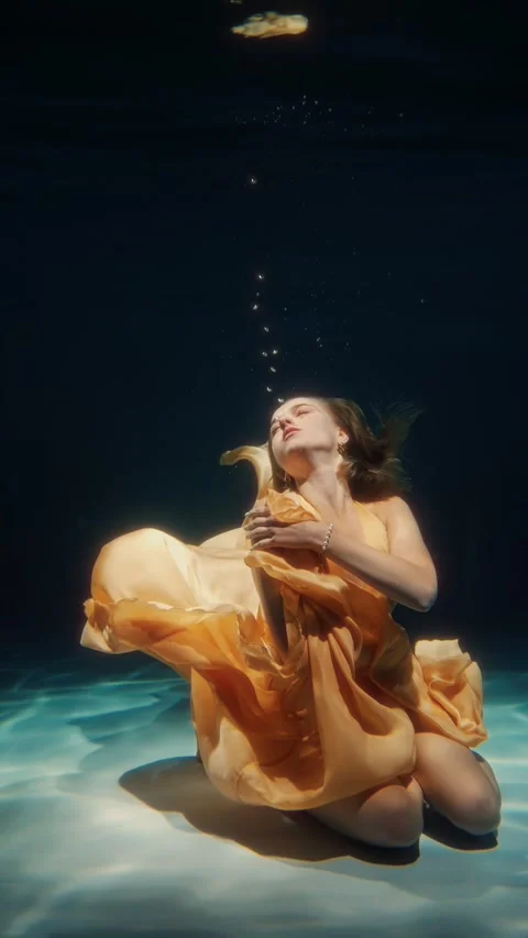 A dancer elegantly moves underwater, adorned in a flowing orange dress 스톡 동영상 315084368