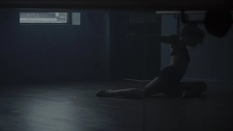 Dancer on the floor warming up and stretching in dark moody dance studio Vidéo 104273659