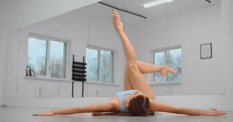 Dancer is lying on the floor of ballet studio and makes warm up exercises for Stock Footage 145074567