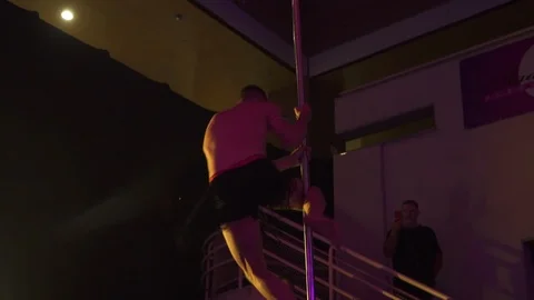 Dancer performing pole dance in club, spins on a pole with purple background Stock Footage 121461432